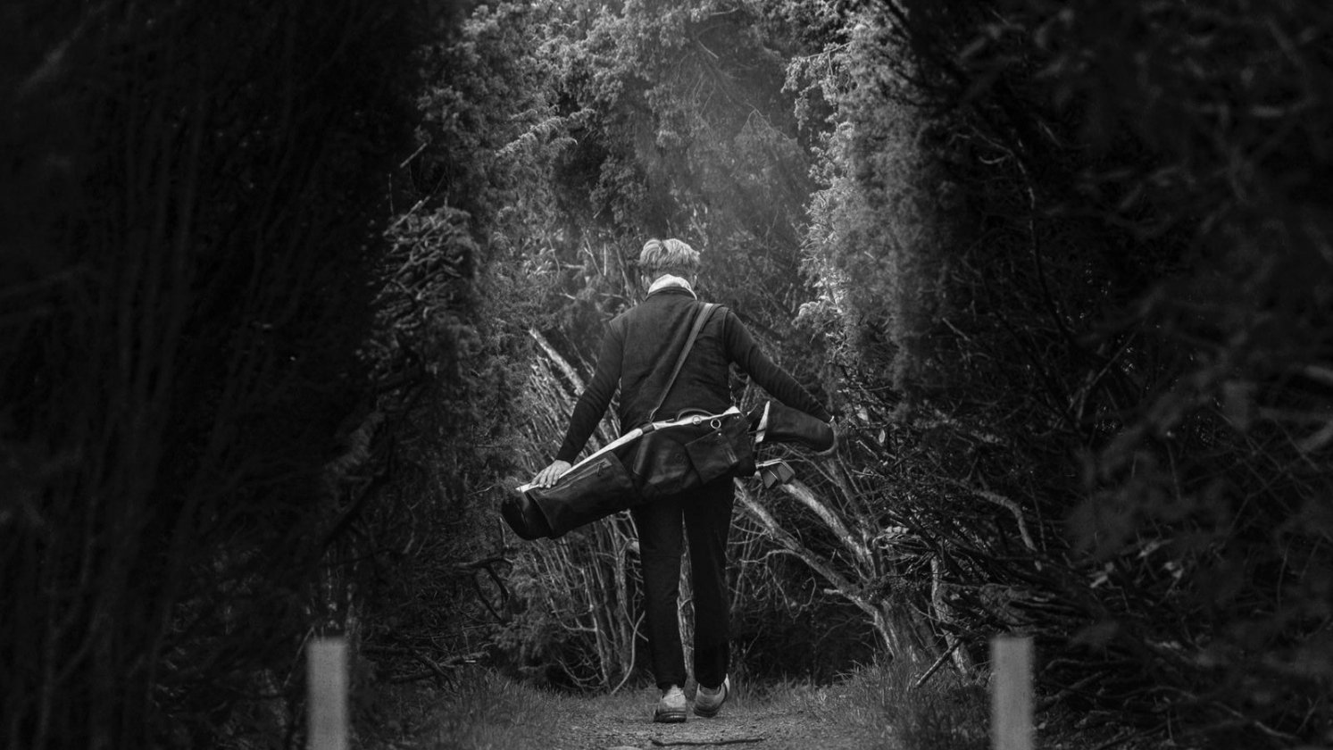 Golfista caminando por un sendero entre árboles con una bolsa de transporte Pine Coast al hombro